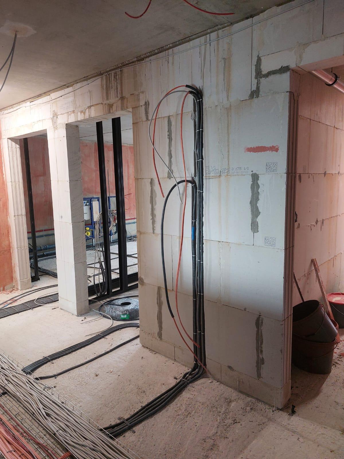 Surowy stan budynku w trakcie prac: widoczne przewody elektryczne prowadzone po ścianach z betonu komórkowego, kable ułożone na podłodze, przygotowane do rozprowadzenia w nowym obiekcie.