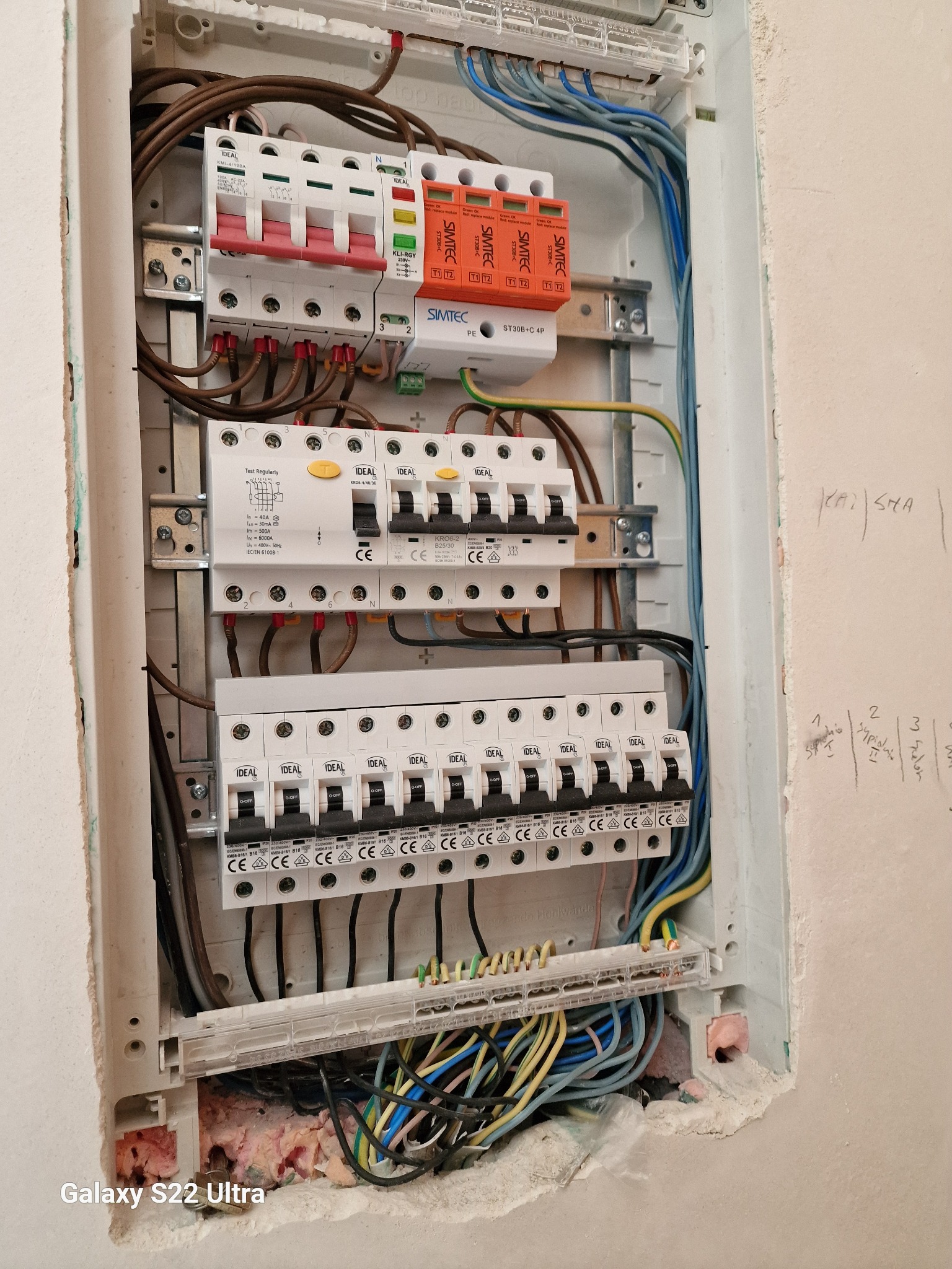 Otwarta skrzynka rozdzielcza z widocznymi bezpiecznikami, przewodami i ogranicznikiem przepięć, zamontowana w ścianie z niedokończonym wykończeniem.