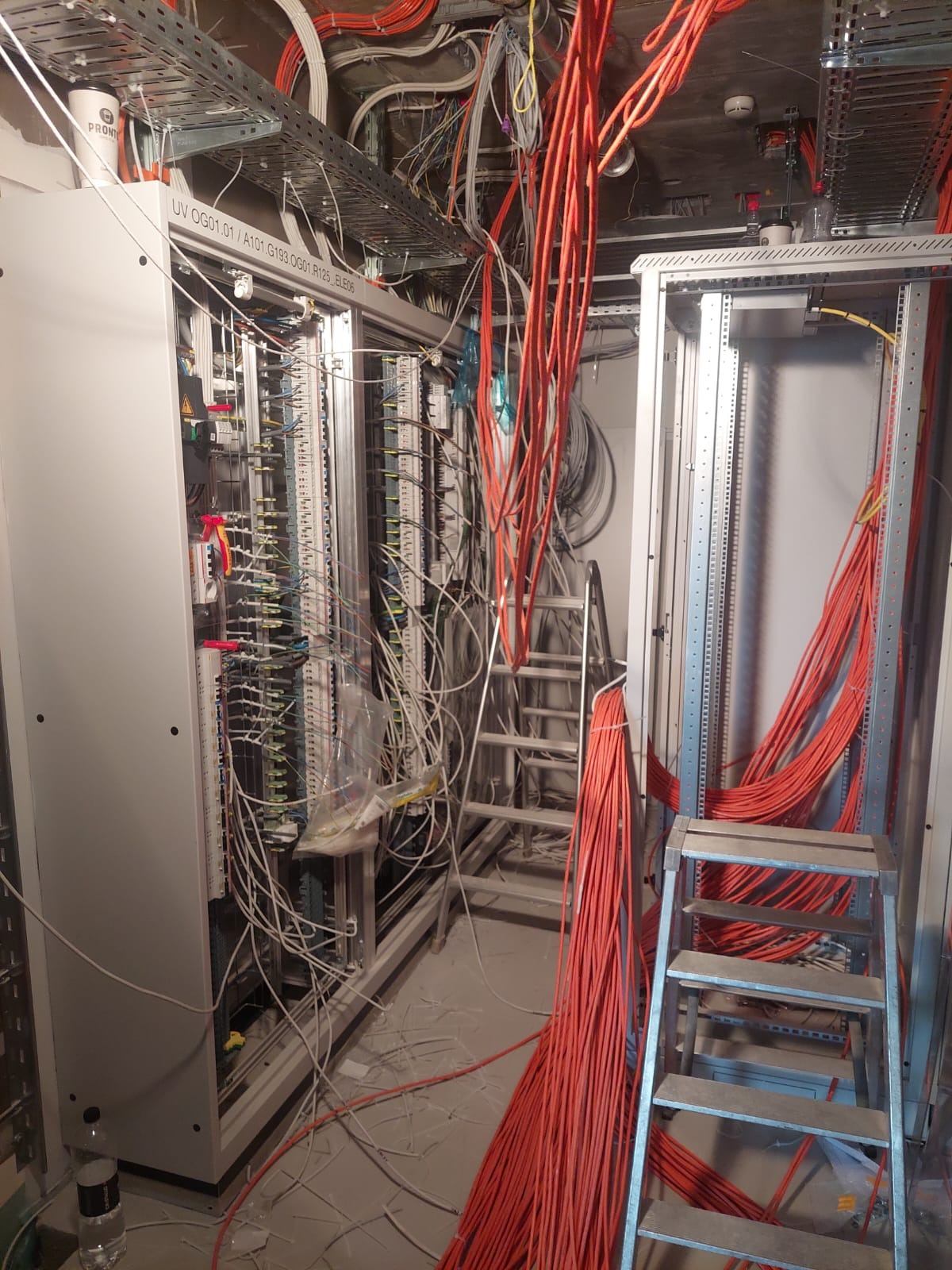 Rozdzielnica elektryczna w trakcie montażu, widoczne liczne przewody, drabina i elementy konstrukcyjne.