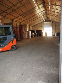 Magazyn z kostką brukową, widok na wózek widłowy i palety z kostką, oświetlony przez światło wpadające z zewnątrz, posadzka z ułożonej kostki brukowej.