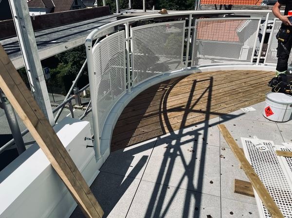 Montaż drewnianego tarasu na dachu z białą, ażurową balustradą, widok z góry, fragment rusztowania w tle.