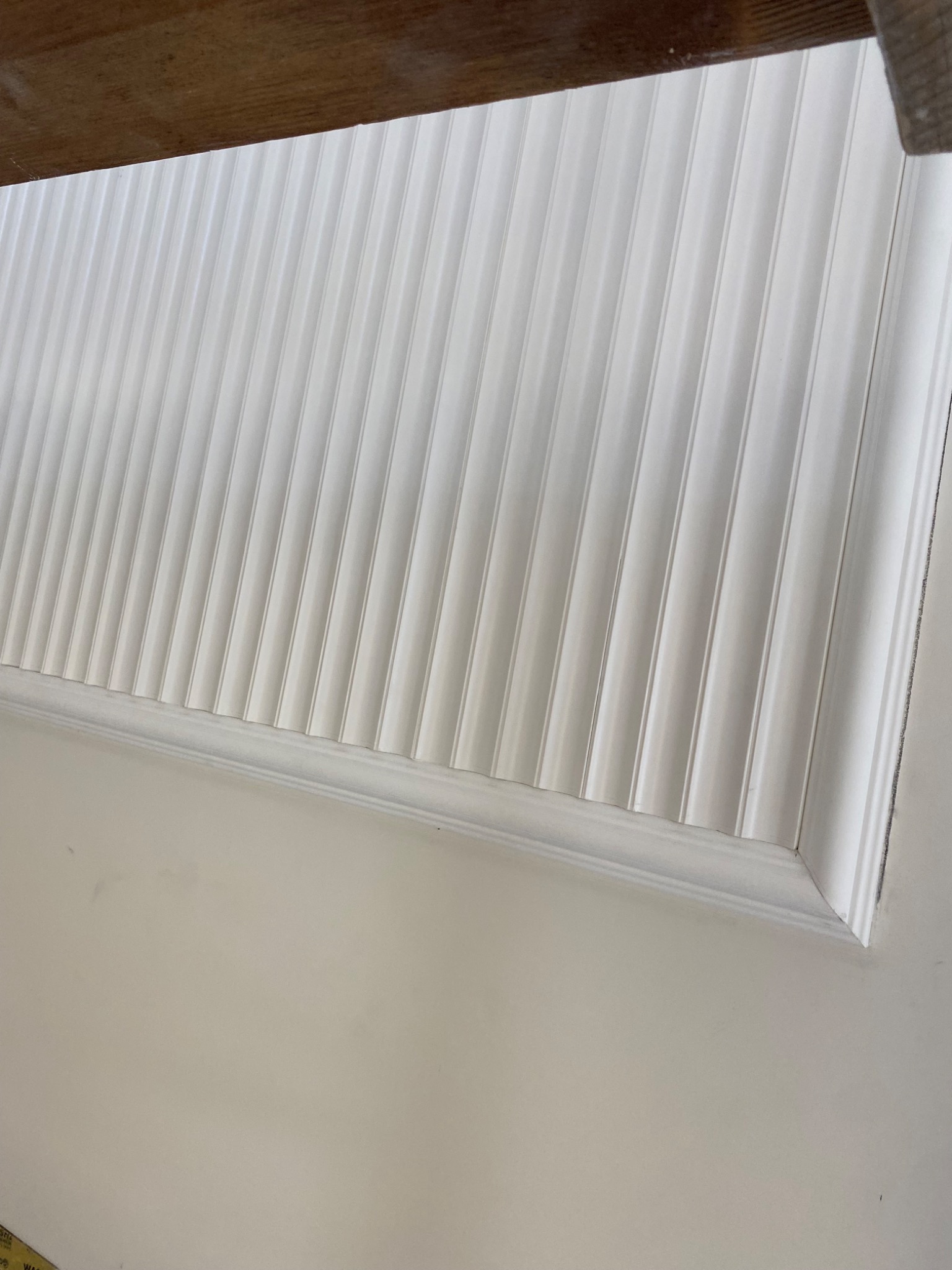 Wykończona ściana z białymi panelami dekoracyjnymi, widoczne pod kątem od dołu, z fragmentem drewnianej konstrukcji u góry.