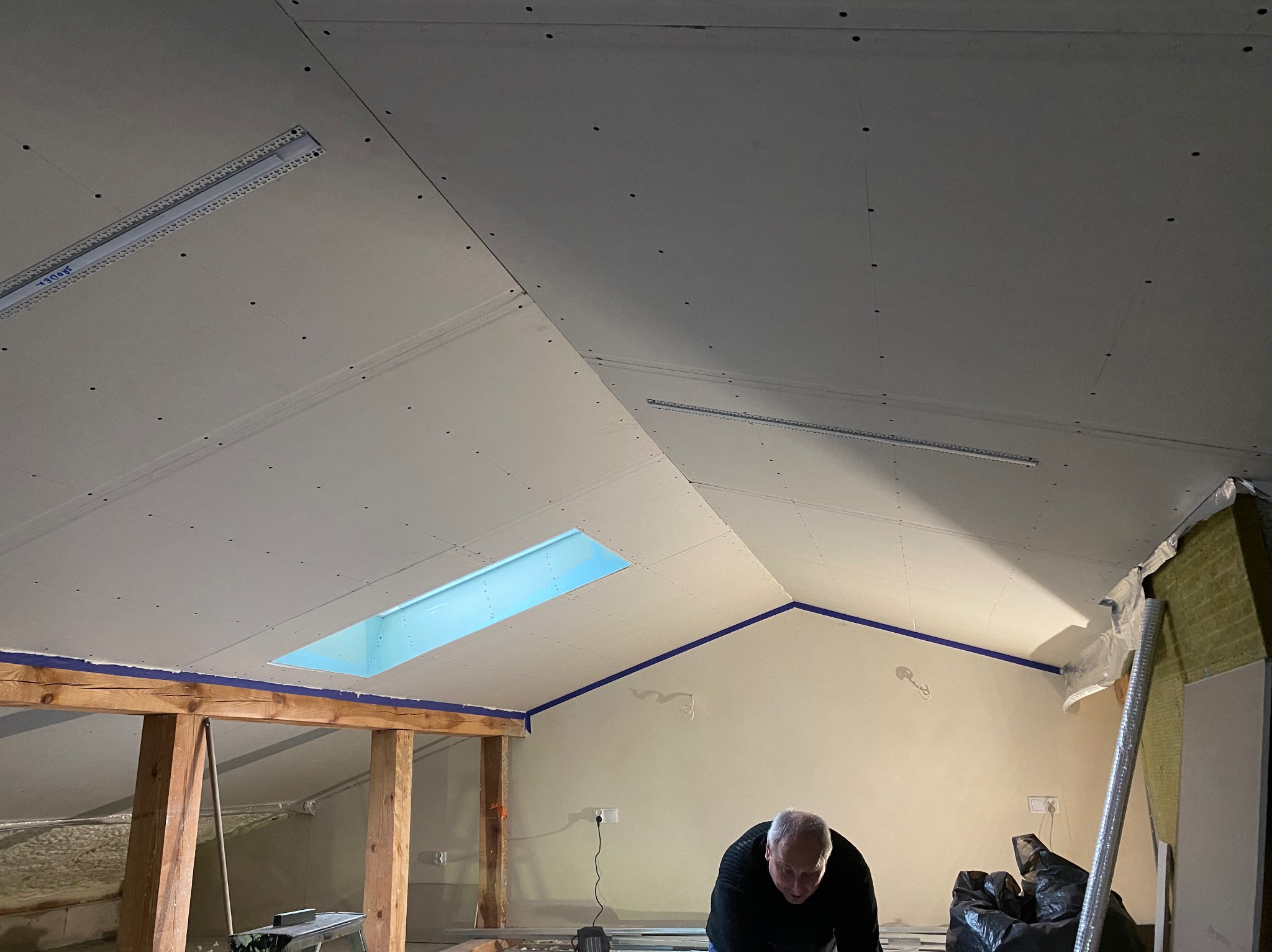 Montaż płyt kartonowo-gipsowych na poddaszu z oknem dachowym; widoczne profile, wkręty i częściowo ocieplona ściana.