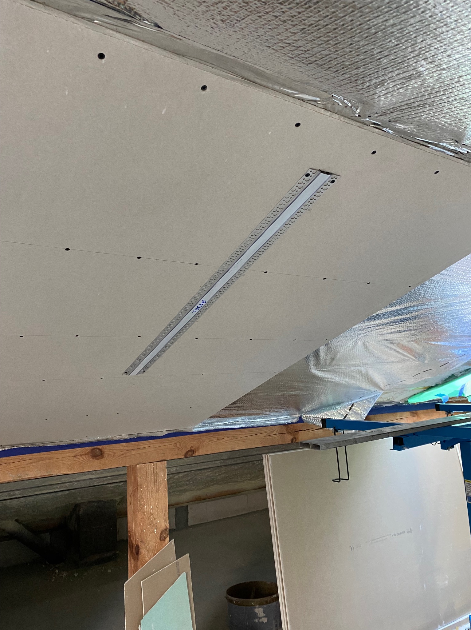 Montaż sufitu podwieszanego: płyty karton-gips mocowane do stelaża, widoczna izolacja termiczna folią aluminiową, szpachlowane łączenia płyt.