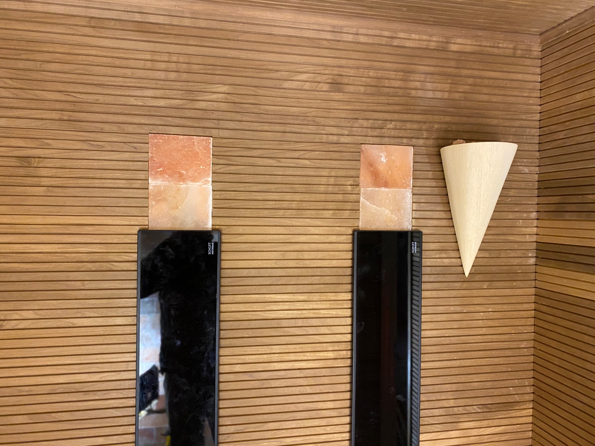 Wykończenie wnętrza sauny z drewnianą boazerią, dwoma czarnymi panelami grzewczymi z blokami soli himalajskiej na górze i drewnianym czerpakiem na ścianie.