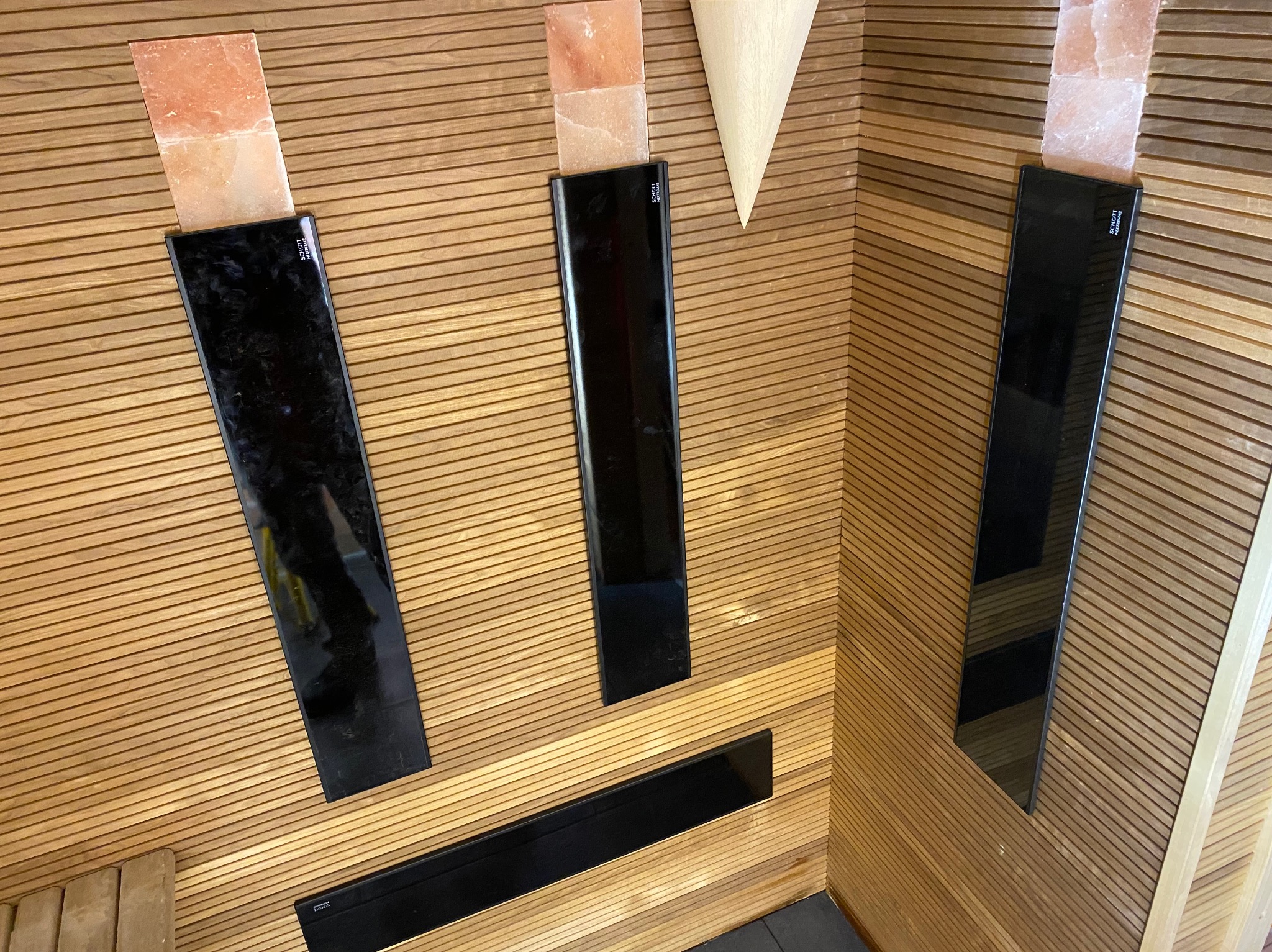 Sauna z drewnianą boazerią, wyposażona w podświetlane panele z blokami soli himalajskiej i dekoracyjnym stożkiem z jasnego drewna.