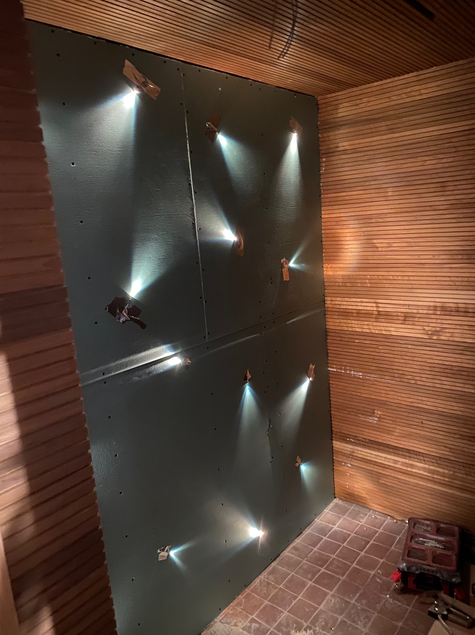 Montaż płyty kartonowo-gipsowej z widocznymi punktami mocowania i taśmą, sąsiadującej z wykończoną drewnianą ścianą i sufitem w pomieszczeniu z terakotą.