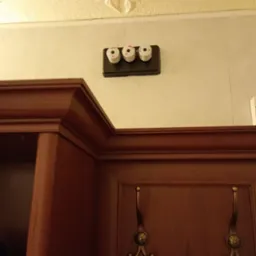 Trzy bezpieczniki topikowe zamontowane na czarnej listwie na ścianie, widoczne nad drewnianą szafką z wieszakami w pomieszczeniu z dekoracyjnym sufitem.