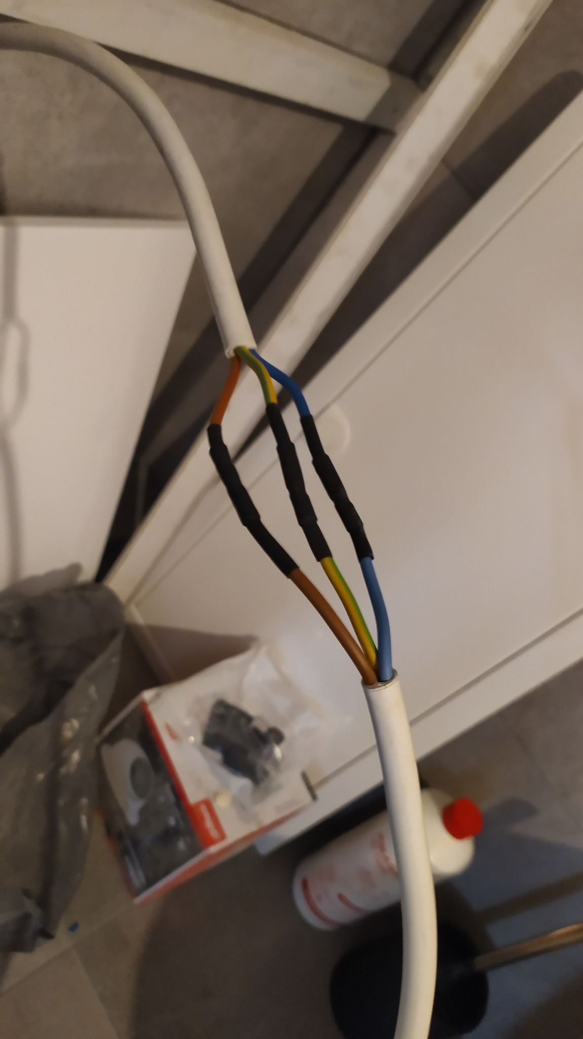 Połączenie przewodów elektrycznych w izolacji termokurczliwej, widoczne kolory: brązowy, żółto-zielony i niebieski, tło stanowią elementy wyposażenia wnętrza.