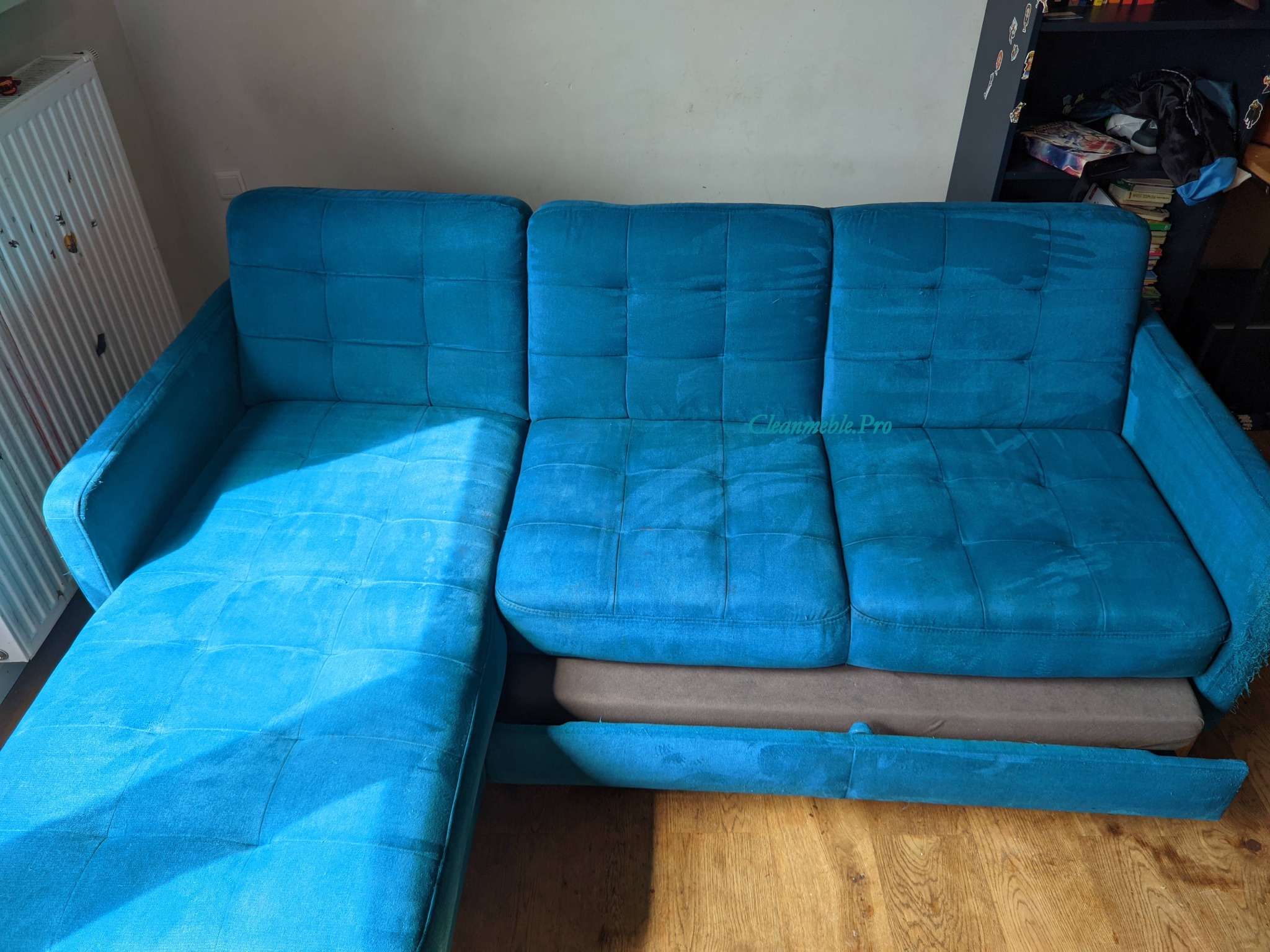 Turkusowa, rozkładana kanapa z widocznymi plamami po czyszczeniu na siedzisku i boku. Widoczny wysunięty element.