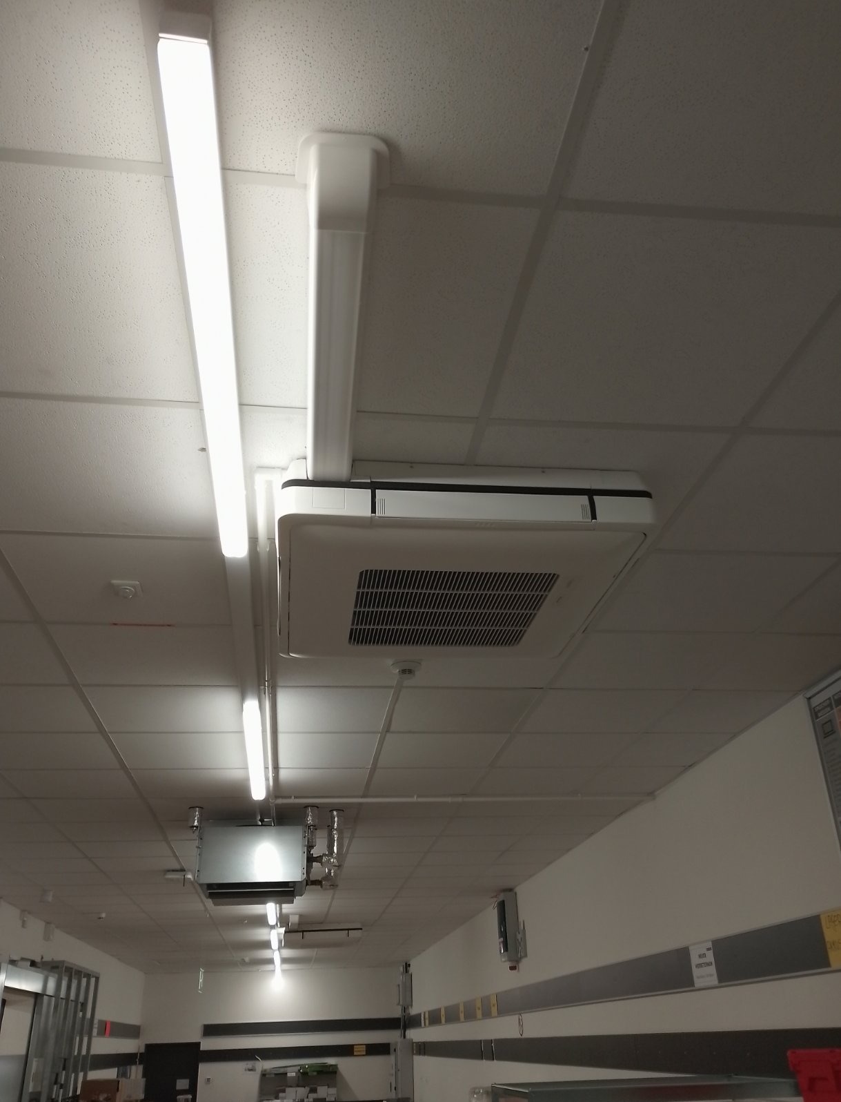 Klimatyzator kasetonowy zamontowany w suficie podwieszanym biura, widoczne oświetlenie LED i instalacje.
