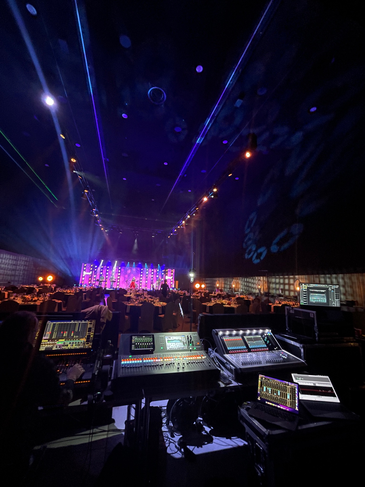 Widok zza konsolety dźwiękowej na scenę z oświetleniem LED i dekoracjami podczas wydarzenia w dużej sali bankietowej.