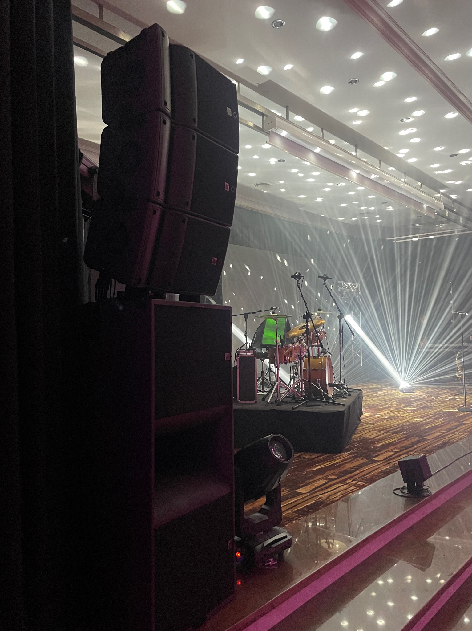 Scena z zestawem perkusyjnym podświetlona reflektorami, widoczne kolumny głośnikowe i oświetlenie sceniczne.