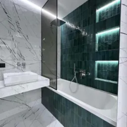 Nowoczesna łazienka z marmurowymi płytkami i zielonymi, podświetlonymi niszami nad wanną, minimalistyczna umywalka nablatowa.