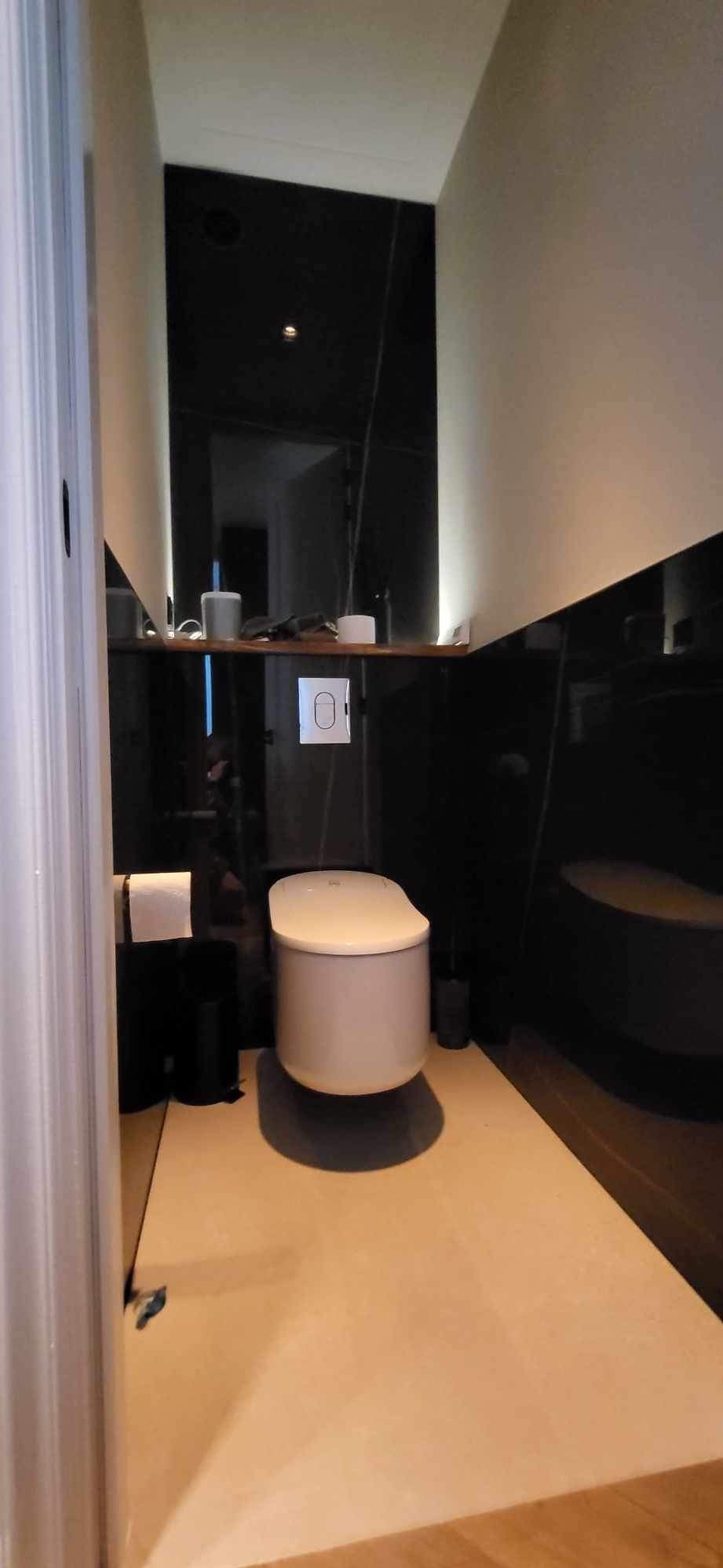 Nowoczesna toaleta w łazience z czarnymi, błyszczącymi ścianami i jasną podłogą, minimalistyczny design z podświetleniem półki.