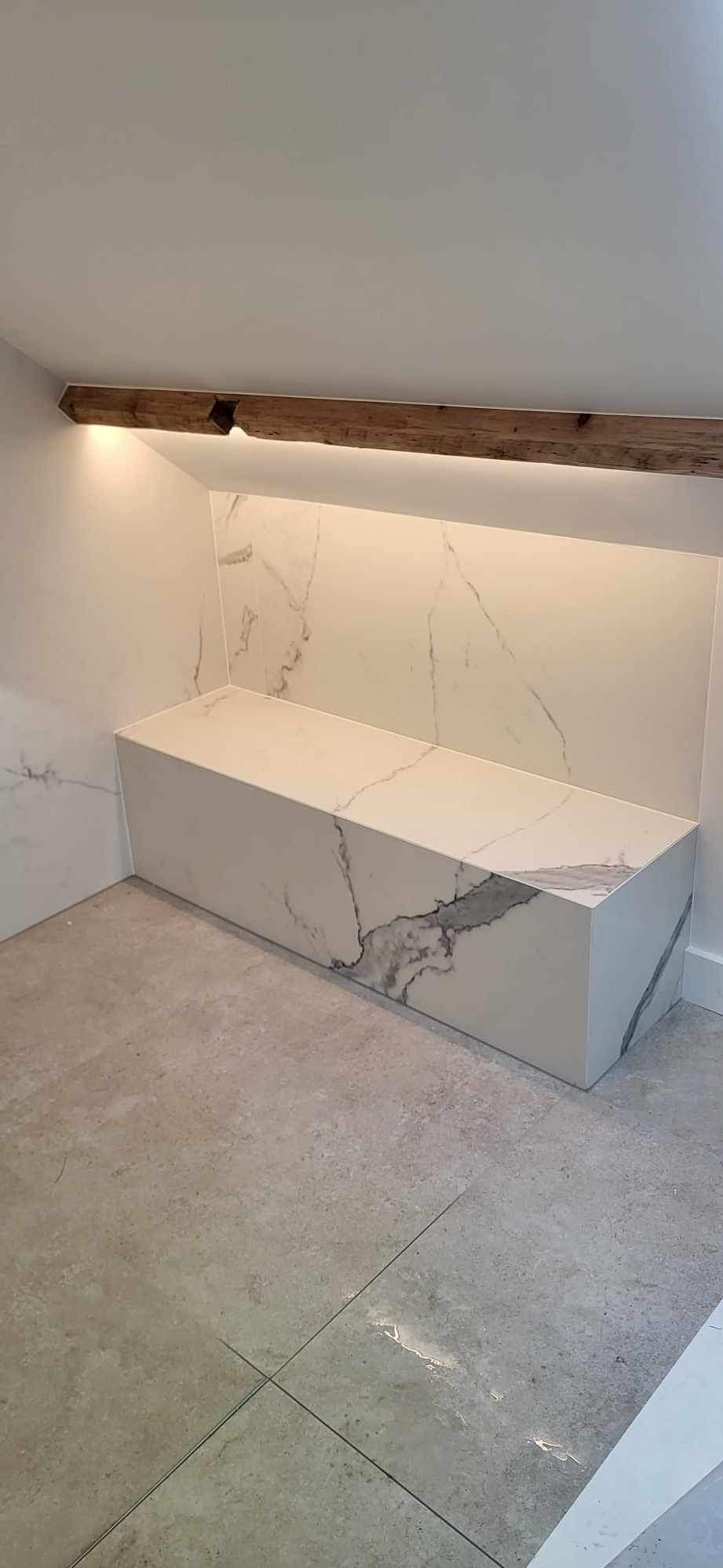 Nowoczesna łazienka z zabudową z płytek imitujących marmur, podświetlona drewniana belka pod sufitem, szara płytka podłogowa