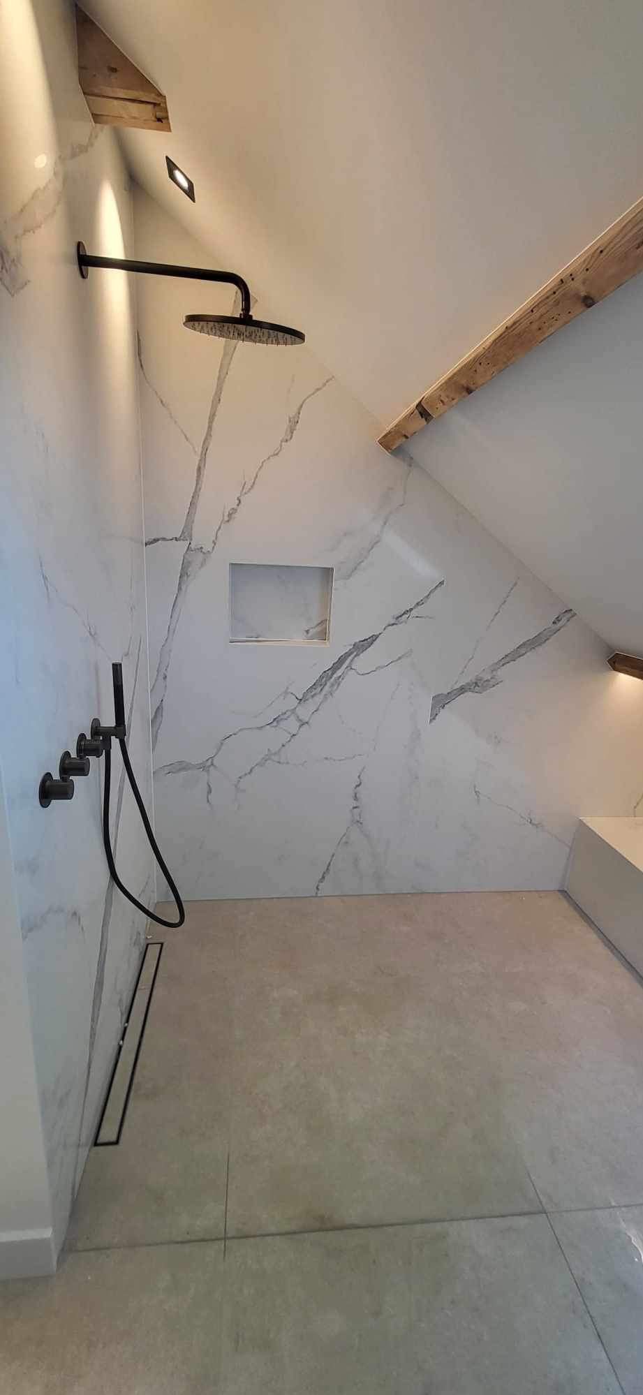 Nowoczesna kabina prysznicowa w skosie z czarną armaturą, płytkami imitującymi marmur i odpływem liniowym.