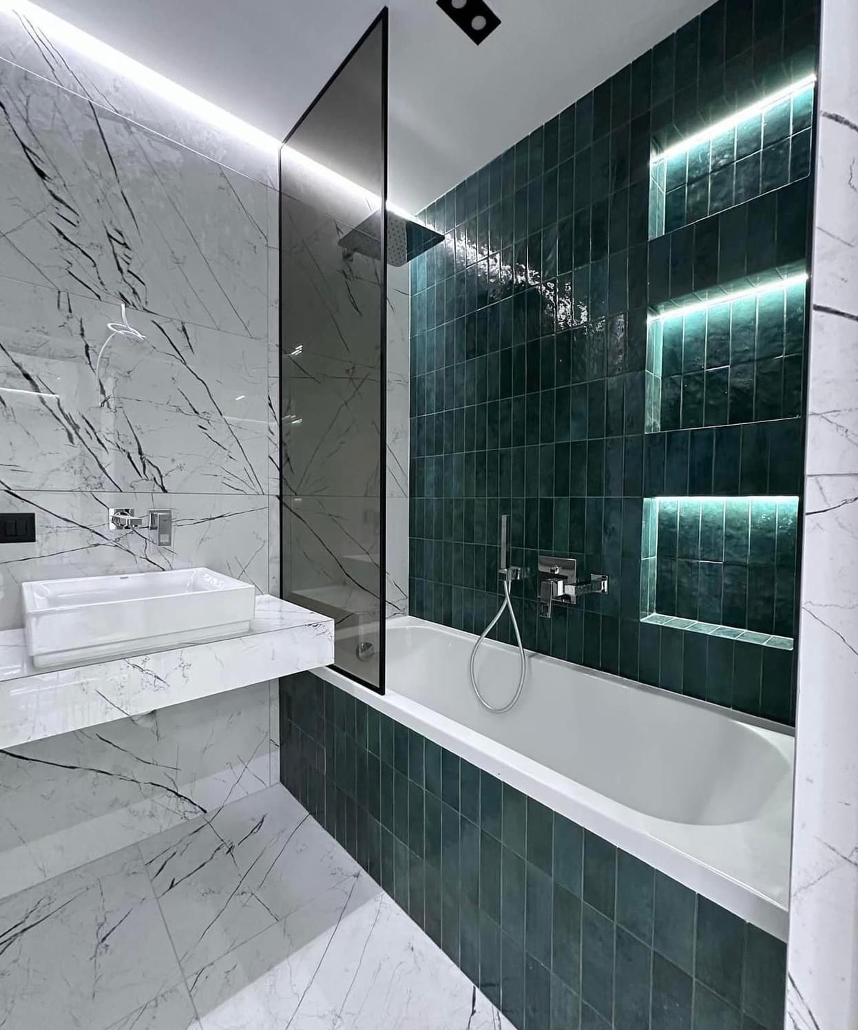 Nowoczesna łazienka z marmurowymi płytkami i zielonymi, podświetlonymi niszami nad wanną, minimalistyczna umywalka nablatowa.