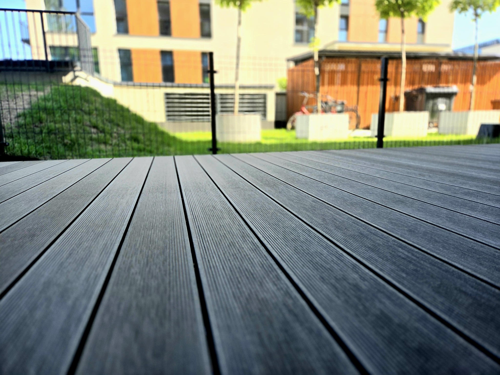 Nowoczesny taras kompozytowy z desek w odcieniach szarości, z widokiem na architekturę miejską Zubrzyca Górna. Minimalistyczny design i trwałe materiały.