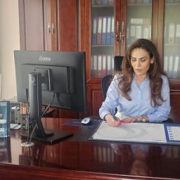 AMK UBEZPIECZENIA WOŁOMIN Agnieszka Kaczyńska - Kobieta w biurze, podpisuje dokument na biurku z kalendarzem, widoczny monitor i broszura Defend Insurance Group