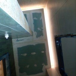 A&ŁREMO - Ściana z płyt gipsowo-kartonowych w trakcie przygotowania do dalszych prac wykończeniowych, widoczne łączenia płyt pokryte masą szpachlową, oświetlenie LED wzdłuż ściany.