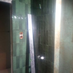 A&ŁREMO - Montaż pionowych, błyszczących, zielonych płytek w łazience, widoczna poziomica przy ścianie, otwory na gniazdka i brakujące fragmenty fugi.