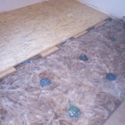 A&ŁREMO - Izolacja podłogi wełną mineralną i montaż płyt OSB na legarach w trakcie remontu w Rudzie Śląskiej, widoczne niebieskie elementy mocujące.