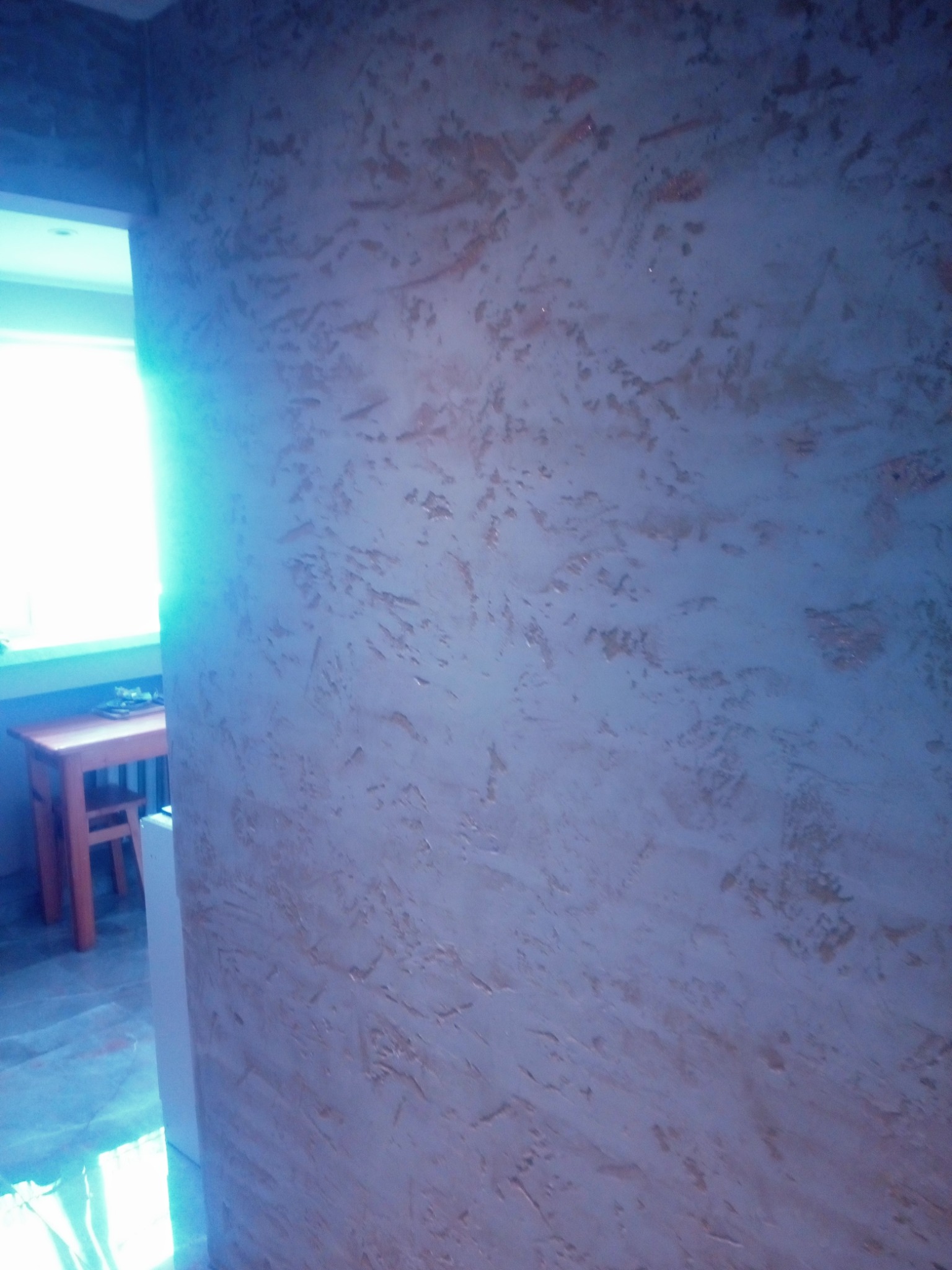 Dekoracyjna ściana z efektem strukturalnym w odcieniach beżu i szarości, widoczny fragment pokoju z oknem w tle.