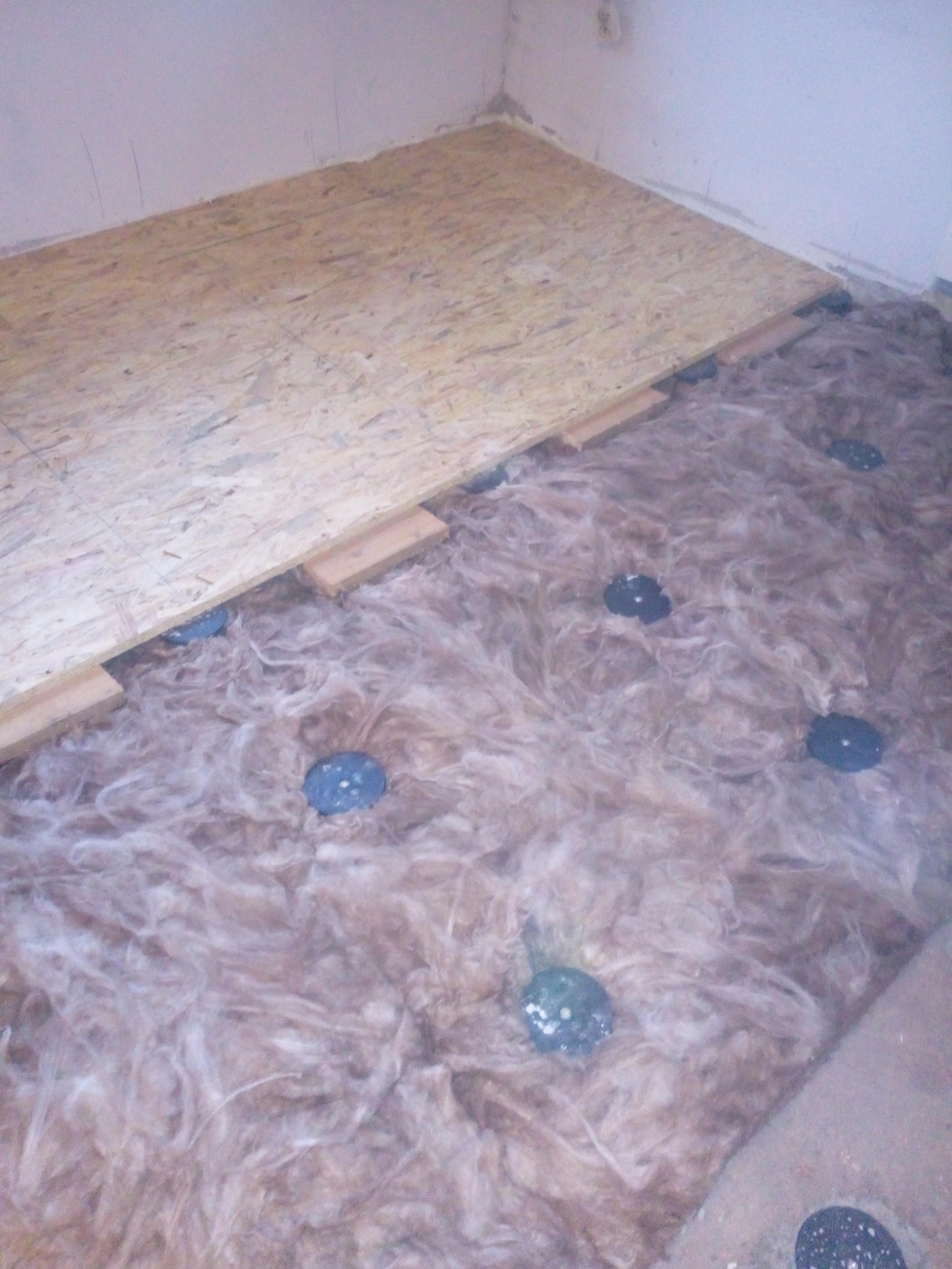 Izolacja podłogi wełną mineralną i montaż płyt OSB na legarach w trakcie remontu w Rudzie Śląskiej, widoczne niebieskie elementy mocujące.