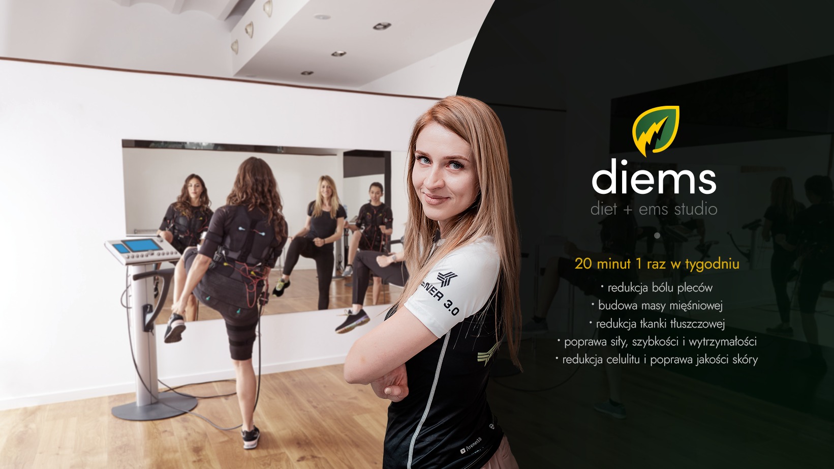 Uśmiechnięta kobieta na pierwszym planie, w tle grupa osób ćwiczących w kombinezonach EMS w przestronnym studiu z lustrami.