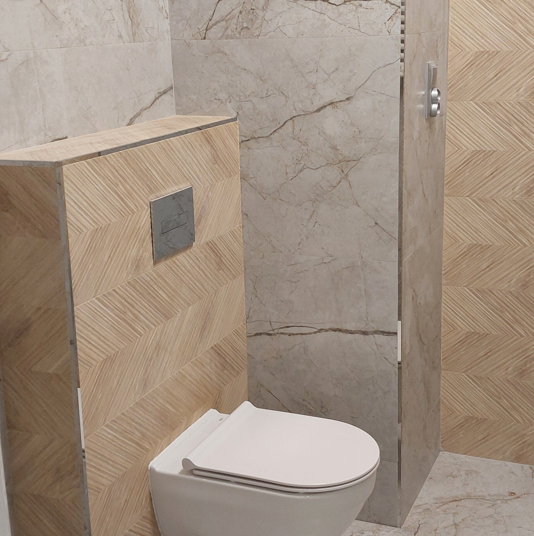Podwieszana toaleta z zabudową w geometryczny wzór drewna, na tle marmurowych płytek w beżowej tonacji, widoczny panel sterujący spłukiwaniem.