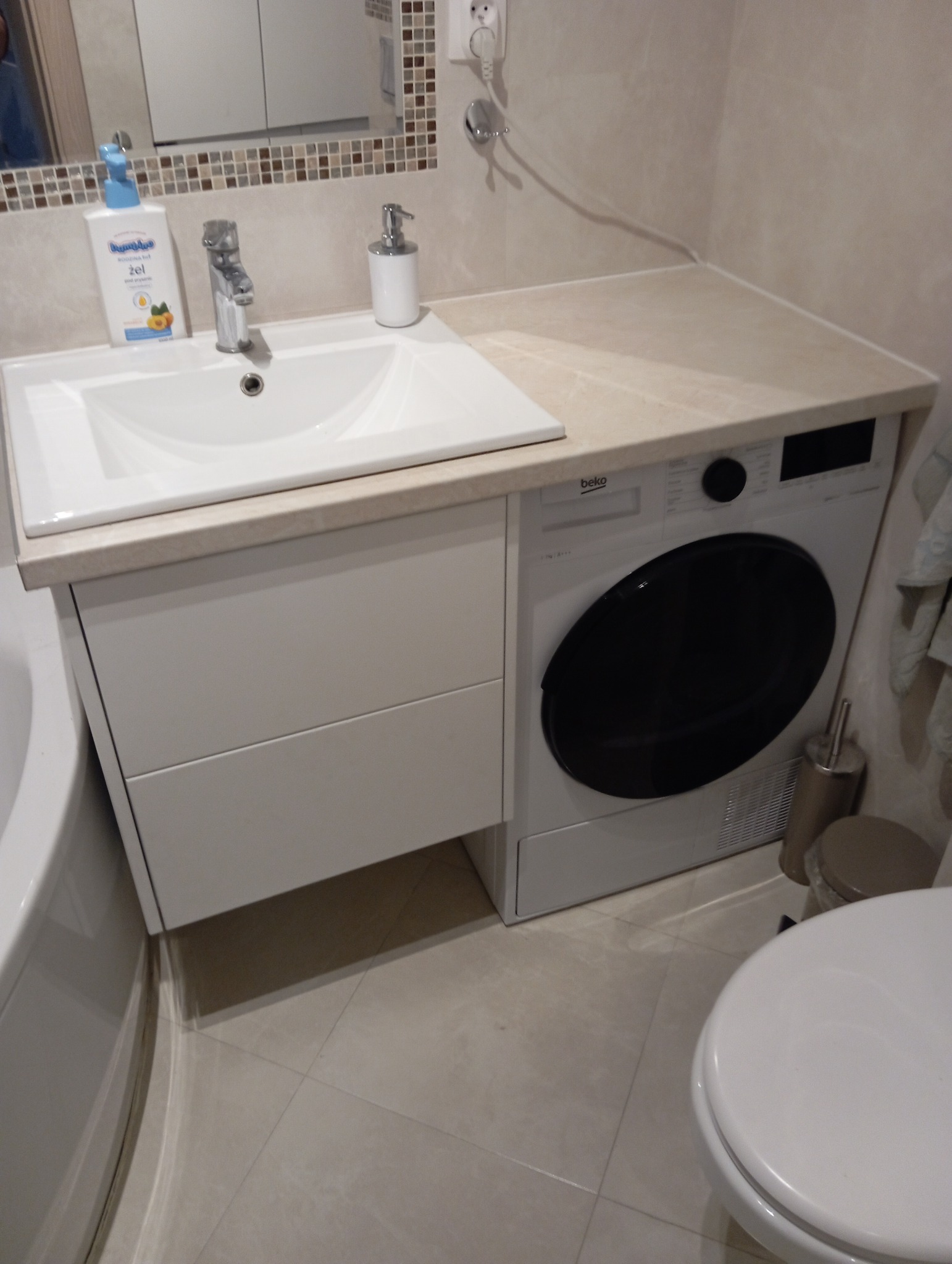 Biała szafka łazienkowa na wymiar z umywalką i pralką Beko wbudowaną obok, widok na baterię, dozownik mydła i fragment toalety.