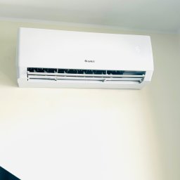 OSD-systemy Klimatyzacji Kraków - Biały klimatyzator Gree zamontowany na jasnej ścianie. Widoczne żaluzje i wyświetlacz temperatury. Minimalistyczny design, czyste linie.