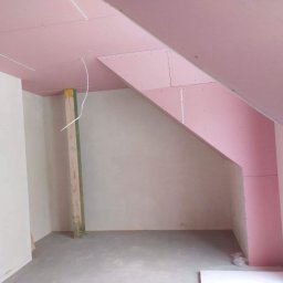 JW construction - Montaż płyt gipsowo-kartonowych na poddaszu, widoczne profile i przewody elektryczne, surowy beton na podłodze, fragment okna w prawym dolnym rogu.