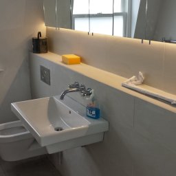 JW construction - Nowoczesna umywalka z baterią i dozownikiem mydła w łazience z jasnymi płytkami, widoczna puszka z farbą i gąbka, prawdopodobnie w trakcie lub po remoncie.