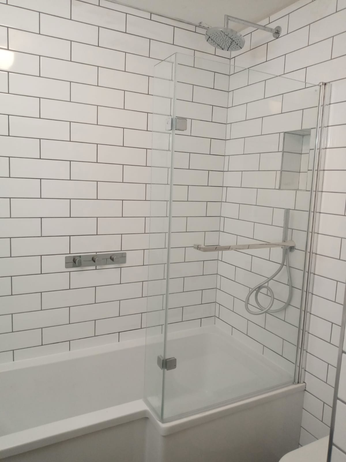 Nowoczesna łazienka z białą, prostokątną glazurą, szklanym parawanem nawannowym i chromowaną armaturą, wnęka w ścianie.