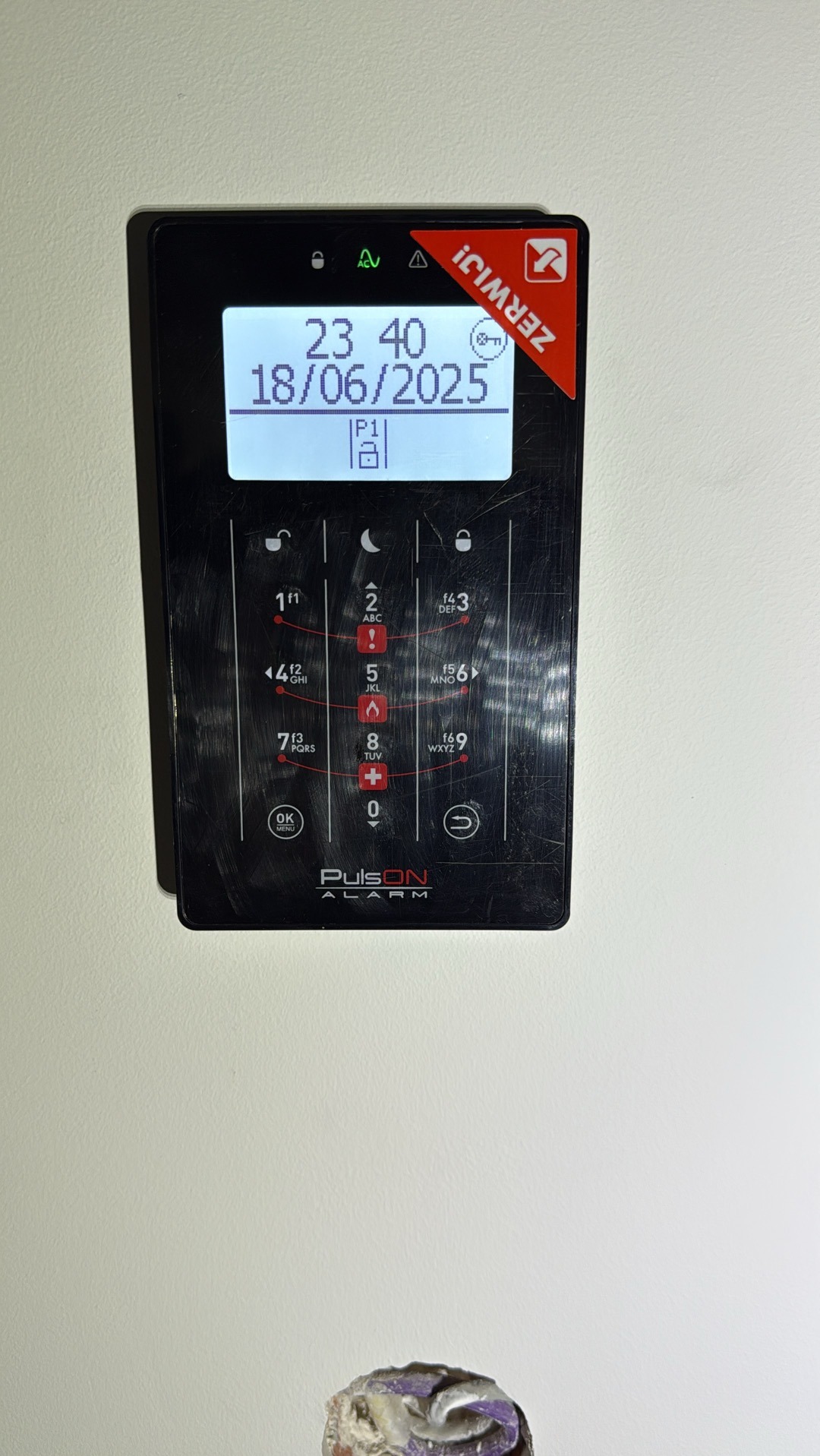 Czarny panel sterowania alarmem PulsON z datą 18/06/2025 i godziną 23:40, zamontowany na białej ścianie, z widocznymi śladami użytkowania.