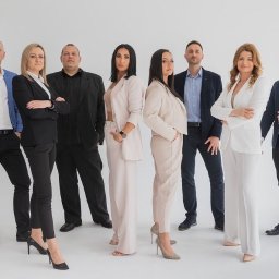 Blue Real Estate Bogacka & Gołębiowska s.c - Grupa ośmiu elegancko ubranych osób, mieszany zespół w garniturach i garsonkach, stojących na białym tle, prezentujących profesjonalizm i pewność siebie, z delikatnym uśmiechem na twarzach.