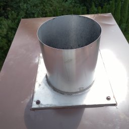 Sebbud - Metalowy komin z kwadratową podstawą, przymocowany do brązowego dachu, widok z góry na tle zieleni.