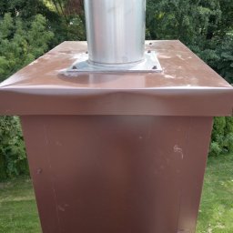 Sebbud - Brązowy komin z metalowym wkładem kominowym na dachu, widok z góry, z zielenią w tle.