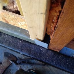 Sebbud - Szczegółowe ujęcie fragmentu konstrukcji szkieletowej z widoczną izolacją, elementami drewnianymi oraz blachą osłonową, narzędzia dekarskie i wkrętarka leżące obok.