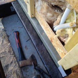 Sebbud - Fragment konstrukcji szkieletowej z izolacją z wełny mineralnej i przewodami elektrycznymi, widoczne narzędzia: siekiera z czerwoną rękojeścią, nożyce do blachy i wkrętarka