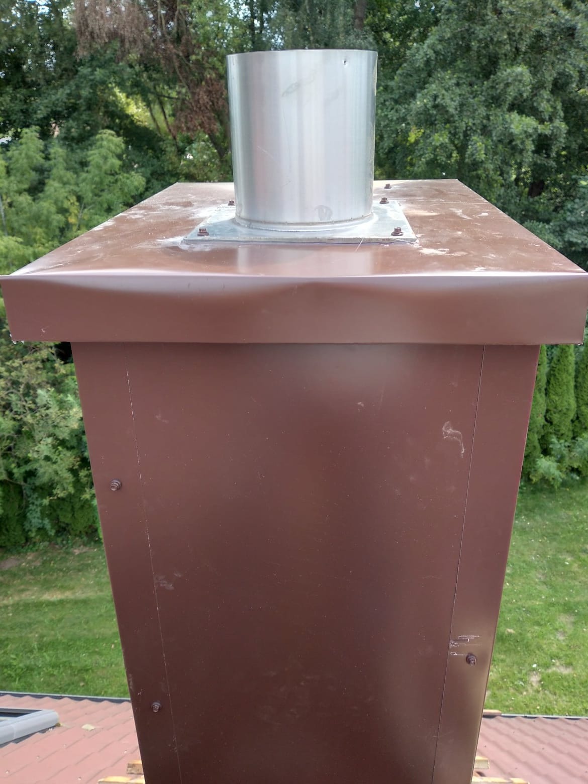 Brązowa obróbka blacharska komina z metalowym wkładem, widoczne ślady zabrudzeń na górnej powierzchni.