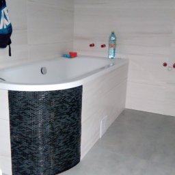 Patryk Cieślak - Nowoczesna łazienka z wanną w zabudowie mozaiką, płytki gresowe na ścianach i podłodze. Widoczne przyłącza hydrauliczne i butelka wody mineralnej.