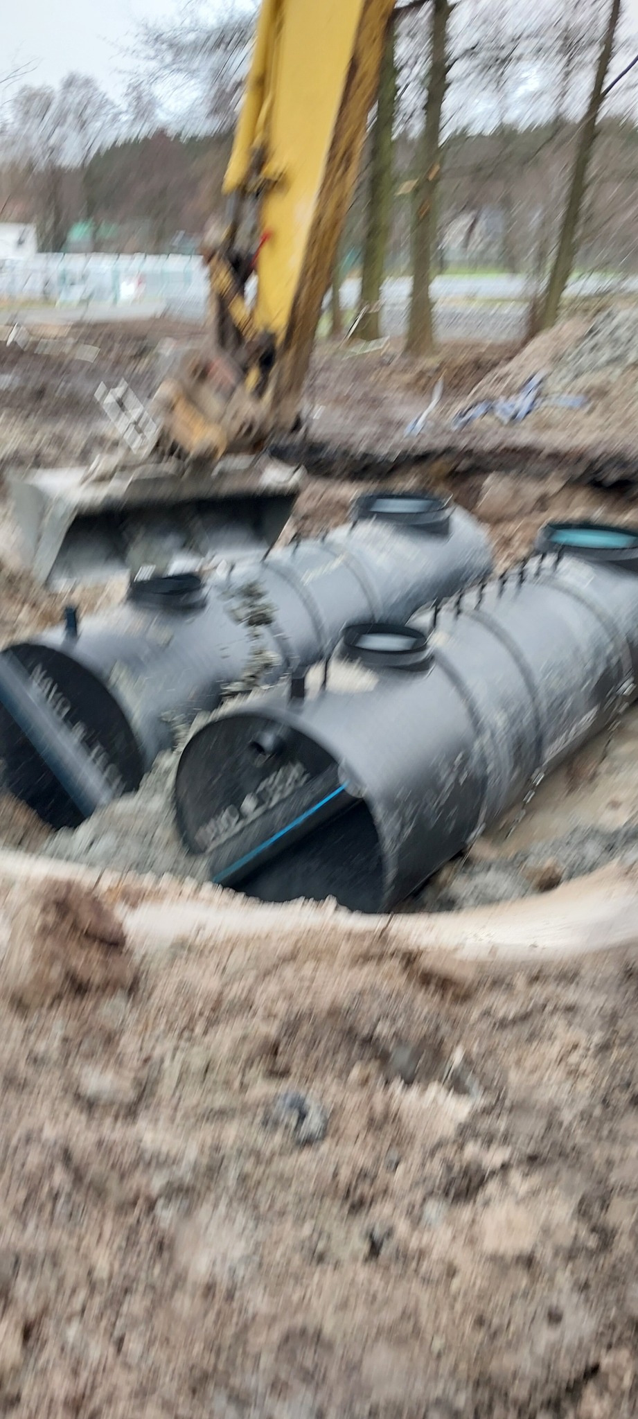 Żywiec: Czarny zbiornik na szambo z żółtą koparką w tle, częściowo zakopany w ziemi.