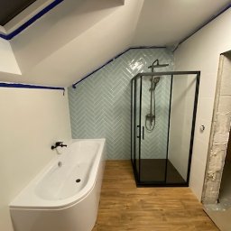 Firma Usługowo-Budowlana - Wykończona łazienka na poddaszu ze skośnym sufitem, z białą wanną narożną, kabiną prysznicową z czarną ramą i błękitnymi płytkami ułożonymi w jodełkę na ścianie.