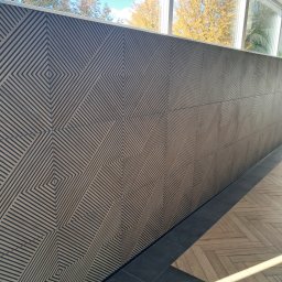 Firma Usługowo-Budowlana - Dekoracyjna ściana z paneli z geometrycznym wzorem rombów, widok z boku, z fragmentem okna i jesiennymi drzewami w tle.