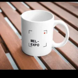 Biały kubek z czarnym logo MEL-EXPO na drewnianym stole z listewek, prezentowany w zbliżeniu.