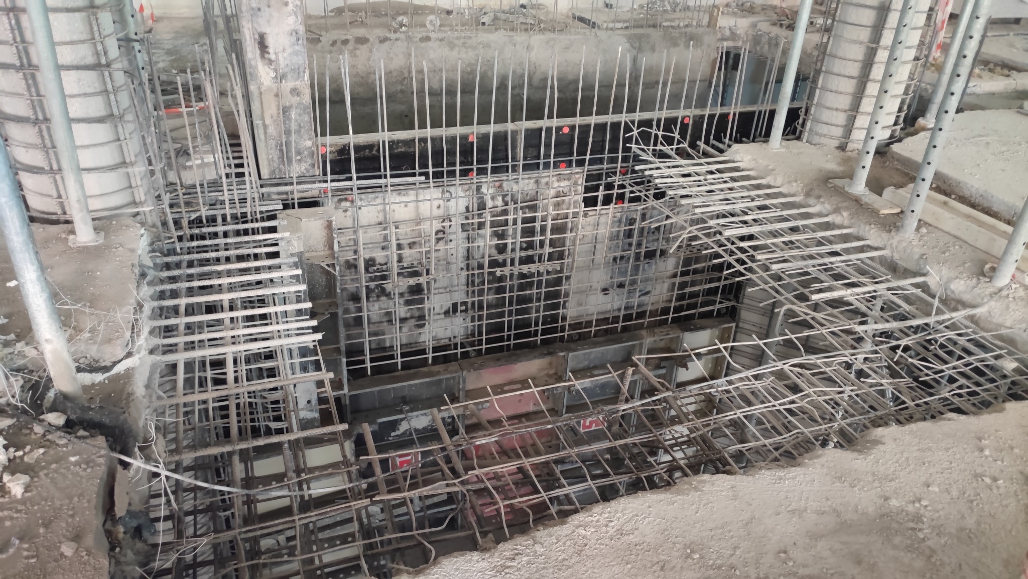 Wykop zbrojony siatką stalową i szalunkami, przygotowany do wylania betonu pod fundamenty budynku. Widoczne pręty zbrojeniowe wystające z górnej części wykopu.