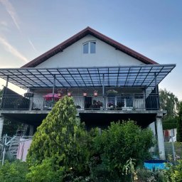 BEE WELD BARTOSZ BYKOWSKI - Dwupiętrowy dom z balkonem z metalowymi balustradami i zadaszeniem z przezroczystego tworzywa sztucznego, widok z ogrodu, z elementami prania na suszarce.